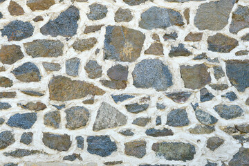 Background of a natural stone or sandstone masonry wall with cement in South France. Detailed stone texture image in beige, brown, grey and blue