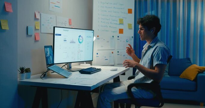 Young Asia male use laptop talk to colleague plan in video call meeting on desk in living room at home office overtime night. Work from house, financial plan, digital nomad job and Gen Z talent.