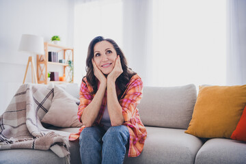 Obraz premium Photo of dreamy cheerful lady wear plaid shirt smiling arms cheeks sitting couch indoors room home house