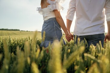 Holding each other's hands. Lovely couple are on the green agricultural field together