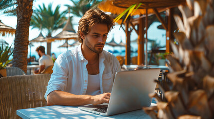 Young man freelancer sitting in beach bar and working on laptop computer. Remote work concept