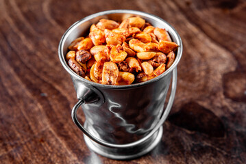A metal cup filled with roasted peanuts on a wooden surface, showcasing the texture and warmth of the snack. Ideal for food and beverage themes, emphasizing rustic and natural elements.