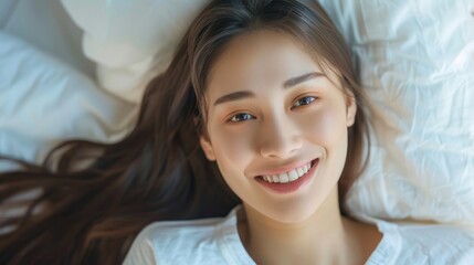 A young woman lying in bed, smiling up at the camera.
