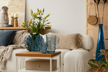 Cozy and boho  living room featuring a white sofa with textured cushions and blankets, a wooden coffee table with decorations, and decorative elements in natural tones. Stylish home interior. Template © FollowTheFlow