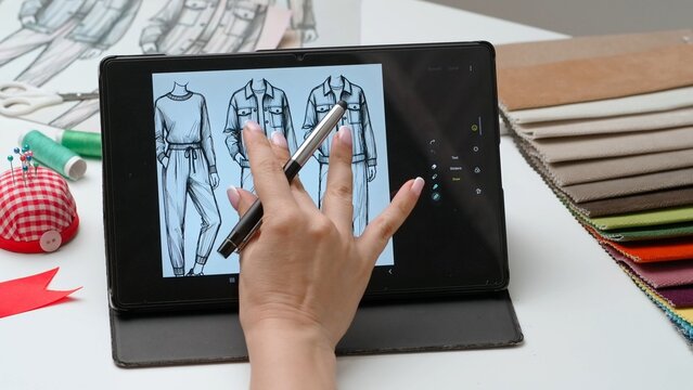 Woman fashion designer works on digital graphic tablet touch screen with illustration of clothing collection sketch. Creativity and modern technology.