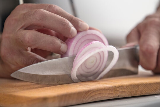 man's hands slicing an onion on wooden cutting board studio shot