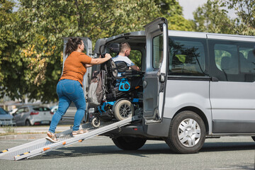 Man with a disability, a wheelchair user getting into an accessible vehicle, with the help of his girlfriend and a ramp for transportation.