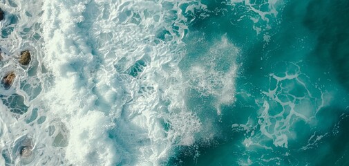 Naklejka premium Aerial view of turquoise ocean waves crashing against rocks, creating white foam and splashes in a dynamic seascape.