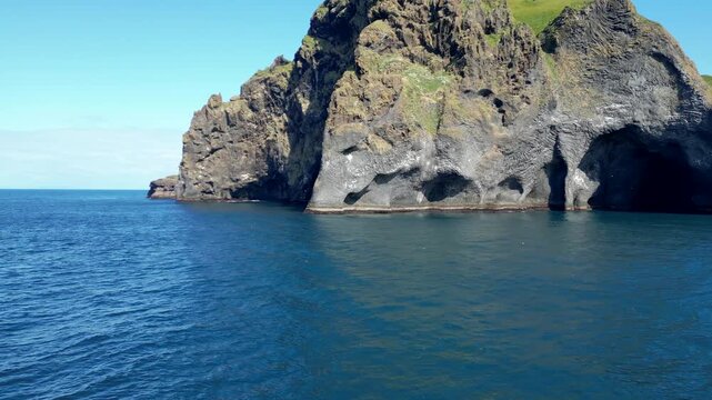 A drone image of Elephant Rock in Iceland. The striking basalt formation resembles an elephant's head dipping into the deep blue ocean, with clear skies adding to the stunning natural beauty.
