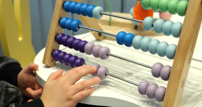 Little child solves maths tasks moving colorful beads on abacus at desk closeup. Toddler boy learns to count with old-fashioned device in preschool class