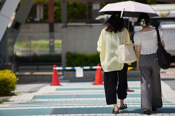 真夏の昼の都市の繁華街で歩く二人の若い女性の姿