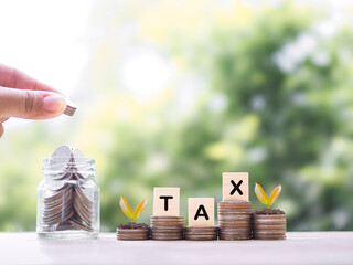 Close up hand putting coin into glass bottle, Wooden blocks with the word TAX on stack of coins. The concept about saving money and manage time to paying tax