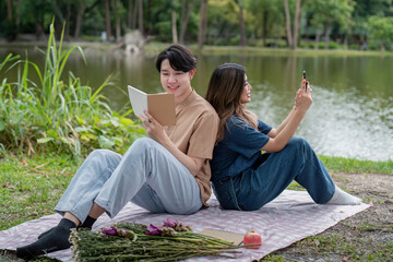 Young Couple Enjoying a Relaxing Picnic by the Lake with Books and Flowers in a Serene Park Setting