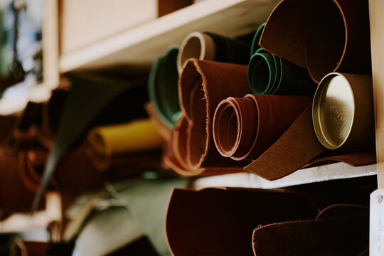 Medium close up of multicolored leather rolls on wooden shelves in workshop