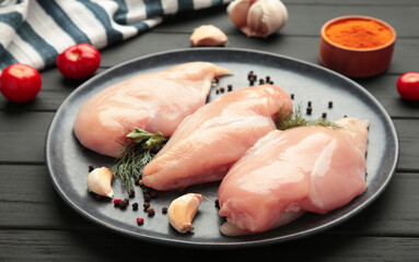 Raw chicken fillet on plate with tomato, spices and dill on black background. Top view
