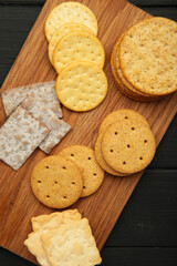 Different crackers on cutting board on black wooden background. Vertical photo
