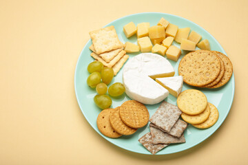 Cheese platter with different cheese and crackers on plate on beige background. Space for text