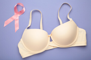 Breast Cancer Awareness Ribbon. Beige bra and pink ribbon tape lying on female bra on purple backgrounds. Breast cancer awareness and October Pink day, world cancer day.