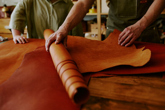Medium close up of unrecognizable male hands rolling out chocolate leather roll while his clients hand touching material