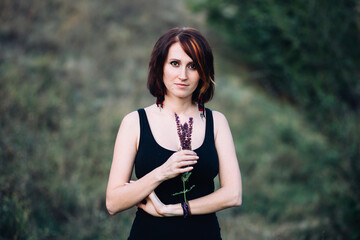 Boho hippie woman with flowers in her hands in nature outdoors on sunset near green hills