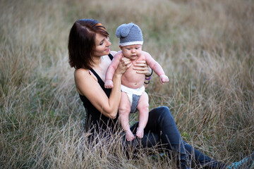 Young mother holding her baby boy in hands, outdoors in summer in sun rays