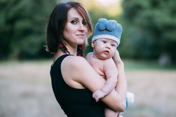 Young mother holding her baby boy in hands, outdoors in summer in sun rays
