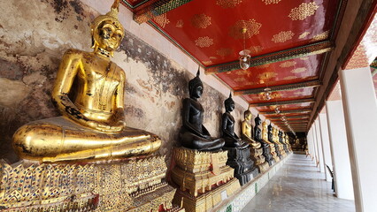 Naklejka premium The gold buddha and black buddha statues inside Wat Suthat Thepwararam, Bangkok. Many sacred Buddha images are enshrined in an old church with beautiful designs. Buddha in meditation pose 