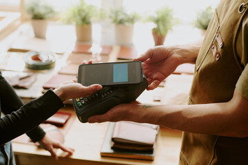 Customer tapping her phone to pay via terminal while male hands holding it