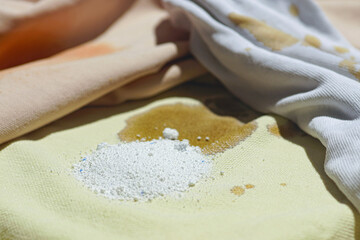 Light cotton clothes with food stains and washing powder scattered on the fabric, close-up photo. Preparing dirty clothes for washing at home.