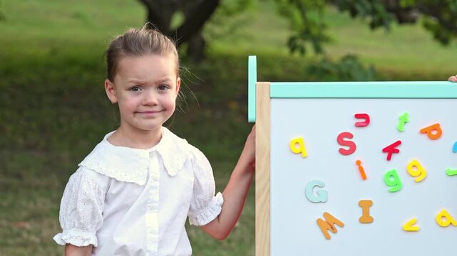 kids are playing in park with blackboard and magnetic letters and numbers attached.colorful blocks, girl and boy sitting on grass lawn.sad disappointed child refuse going back to school.