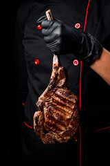 Steak on the bone in the hands of the chef. Prime Black Angus Tomahawk Steak. Close-up. On a black...