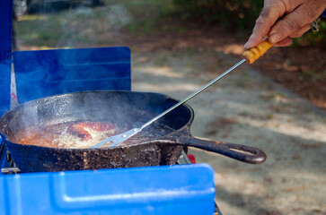 Meat sizzles in hot skillet outdoors