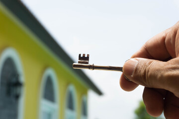 A man's hand holding an old key, the background is a yellow house. Business idea.