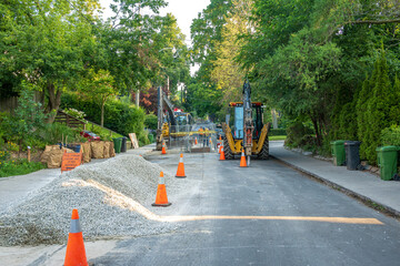 heavy equipment on an older tree lined  residential street repairing infrastructure with piles of gravel and yard waste awaiting collection on the sidewalk shot toronto beaches in summer