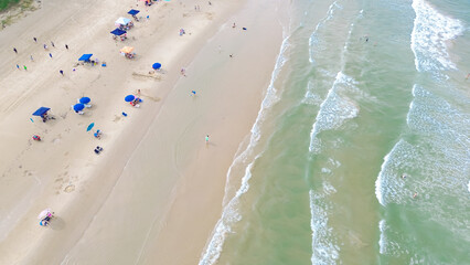Dense of beach umbrella, tent, camping and lounge chairs, diverse people family enjoy swimming, surfing, relaxing with emerald water calm waves at South Beach of Padre Island, Texas, aerial view