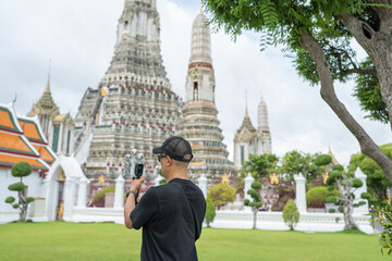 Asian male tourists taking pictures at Wat Arun Temple in Bangkok City, Thailand.