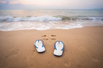 White sandals on the beach in the morning, the sea with white waves.