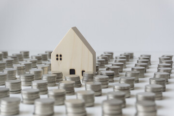 Stacked silver coins And the small white house is between the rows of coins. The concept of saving for buying a house.