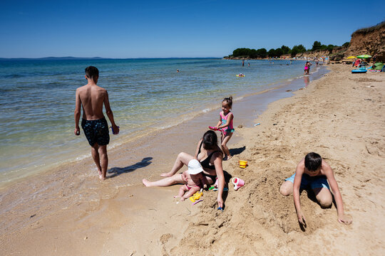 Family enjoying a sunny day at the beach building sandcastles and playing in the water of Croatia.