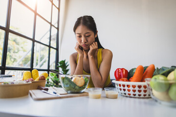 A young Asian woman who eats vegetable salad every day is bored with vegetables. Unhappy women is on dieting time looking vegetable on the fork. girl do not want to eat vegetables and dislike taste.