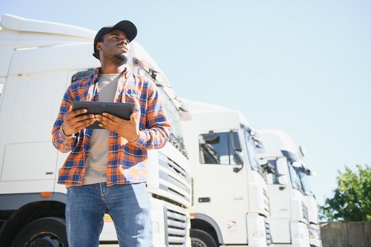 African American professional truck driver setting up navigation for destination. Checking his route on tablet computer and standing by long vehicle. Transportation service