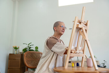 Elderly Woman Painting on Canvas in Bright Minimalist Room with Wooden Furniture and Indoor Plants