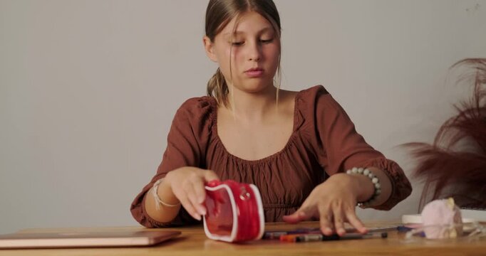 Teenage girl puts school supplies from the table and puts them in a pencil case to pack her backpack and go to school after the holidays. Doing homework at the table.