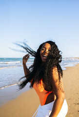 Beautiful African american woman in  bikini on tropical beach. Portrait of dark skinned woman smiling at sea. Brunette tanned girl in swimwear enjoying and walking on beach.