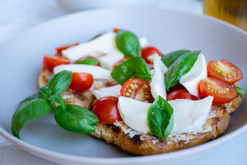 Tomato mozzarella bruschetta with basil close up on white plate - traditional italian appetizer, snack, vegetarian food, healthy eating