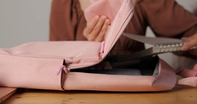 Close-up of a teenage girl hands as she packs her school backpack to go to class. She puts notebooks, a pencil case, a laptop, and other stationery into the backpack. Back to school.
