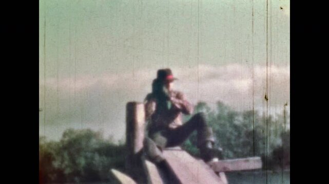 Man cowboy enjoying leisure on river nature background. Carefree man in hat singing songs, tapping by boots outdoor. Relaxed happy rural lifestyle. Vintage color film. Retro western 1960s archive