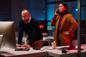 Cybersecurity department in emergency with two people using computers and speaking on phone hacking...