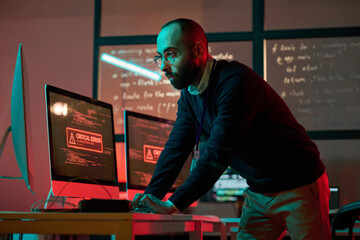 Dramatic portrait of bearded cybersecurity expert preventing emergency and using computer with red...