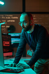 Vertical portrait of bearded cybersecurity engineer working with computer network in blue neon lights © Mediaphotos